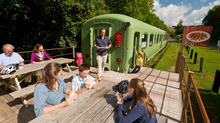 Des gens mangent des gaufres sur des tables en bois à côté d'un wagon de train vert.