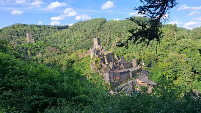 An old castle ruin set in lush green land. In the background, there are hills and a clear blue sky.