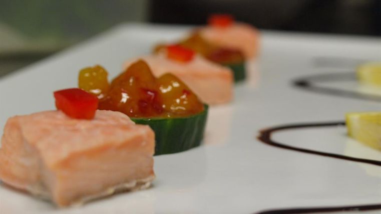 Une œuvre d'art en saumon fumé, servie sur une assiette blanche. À côté du saumon se trouvent des sauces colorées et des légumes frais.