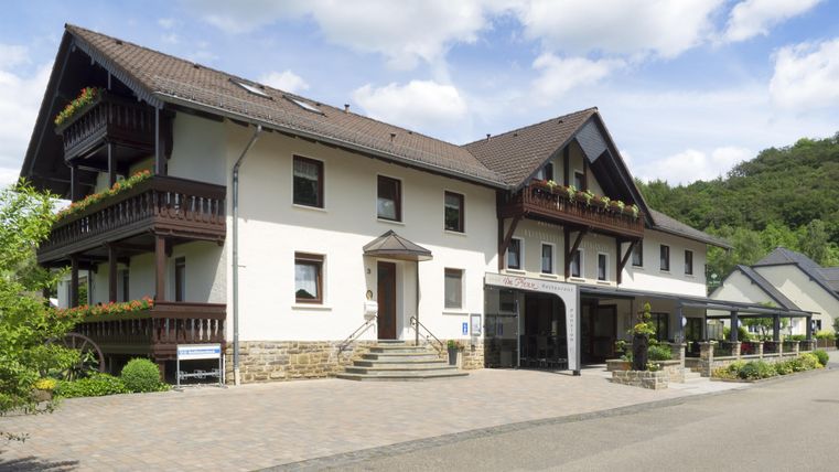 A modern building with balconies, surrounded by green landscape. The sky is blue with some clouds.