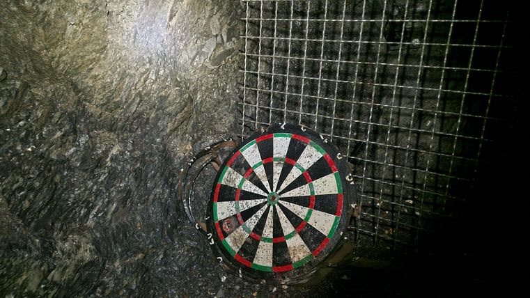 Eine Dartscheibe in einer dunklen Umgebung. Im Hintergrund ist ein Gitter zu sehen.