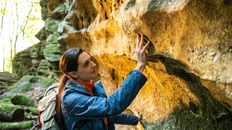 Een vrouw raakt een rots aan in een bos.