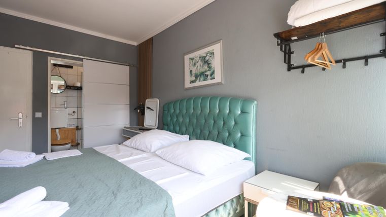 A modern room with a green bed and white bedding. In the background, there is a desk and a equipped bathroom nook.