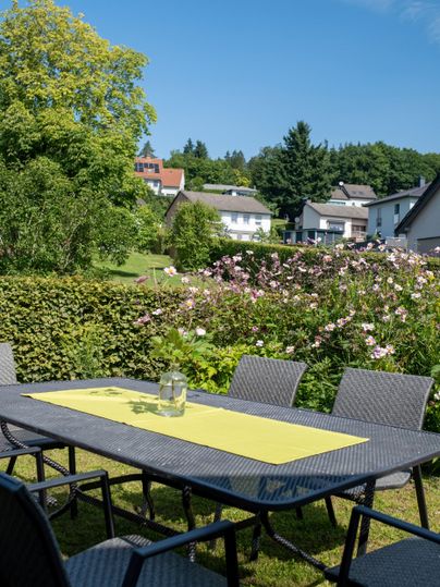 A beautiful garden with a table and chairs. In the background, well-maintained flowers and modern houses can be seen.