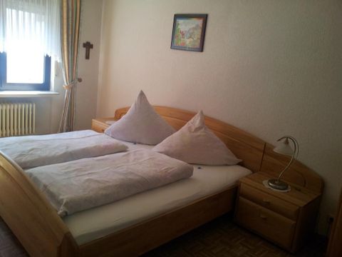 Ein gemütliches Schlafzimmer mit einem Doppelbett und zwei Kissen. Neben dem Bett steht ein Nachttisch mit einer Lampe.