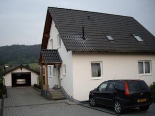 Ein modernes Haus mit einem grauen Dach und einer Auffahrt. Davor steht ein schwarzes Auto und im Hintergrund ist eine Garage zu sehen.