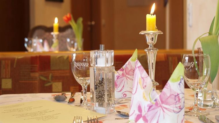 Ein schön gedeckter Tisch mit eleganten Gläsern und dekorativen Servietten. Eine Kerze brennt und frische Blumen verleihen dem Ambiente eine einladende Atmosphäre.