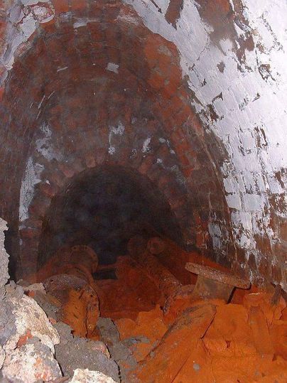 A dark tunnel with discolored walls and loose stones on the floor. The surroundings appear mysterious and eerie.