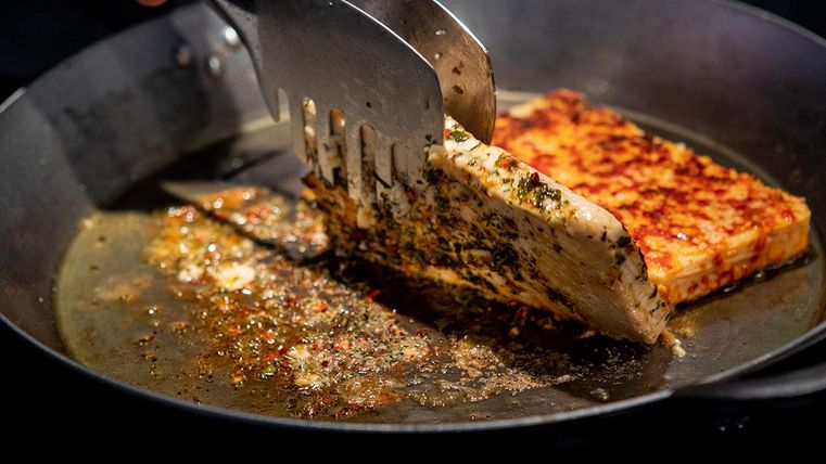 Ein Stück Brat und Grillkäse wird in einer Pfanne gebraten. Leckere Gewürze und eine goldene Kruste sind sichtbar.