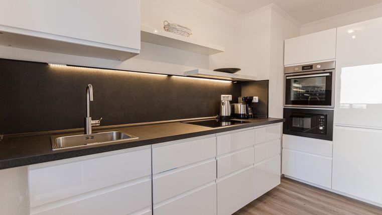Modern kitchen with white furniture and a dark countertop. It is equipped with high-quality appliances and an elegant design.