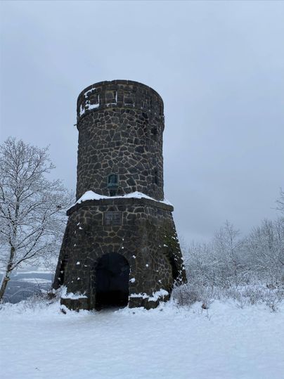 Een oude stenen toren in een besneeuwd landschap. De lucht is grijs en de omgeving is bedekt met sneeuw.
