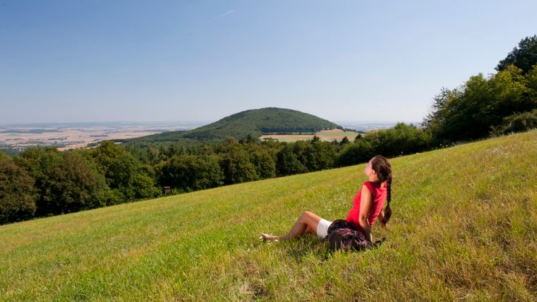 A woman sits in a meadow and looks out over the wooded Hochsimmer.