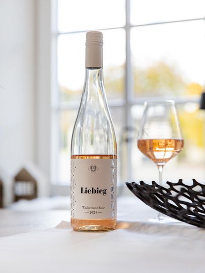 Eine Flasche rosé Wein steht auf einem Tisch neben einem Weinglas. Im Hintergrund sind große Fenster, die natürliches Licht hereinlassen.