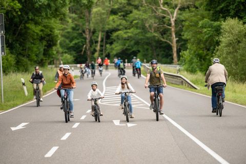 Eine Gruppe von Menschen fährt mit dem Fahrrad auf einer ruhigen Straße. Kinder und Erwachsene genießen einen aktiven Tag in der Natur.