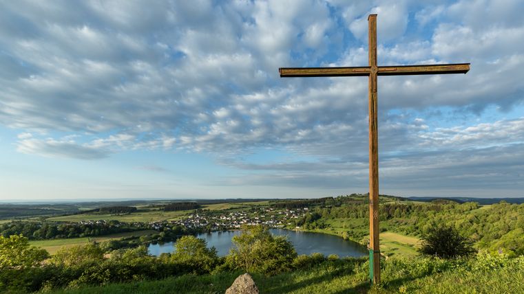 Wooden cross with a view of the Schalkenmehrener Maar and the surrounding landscape.