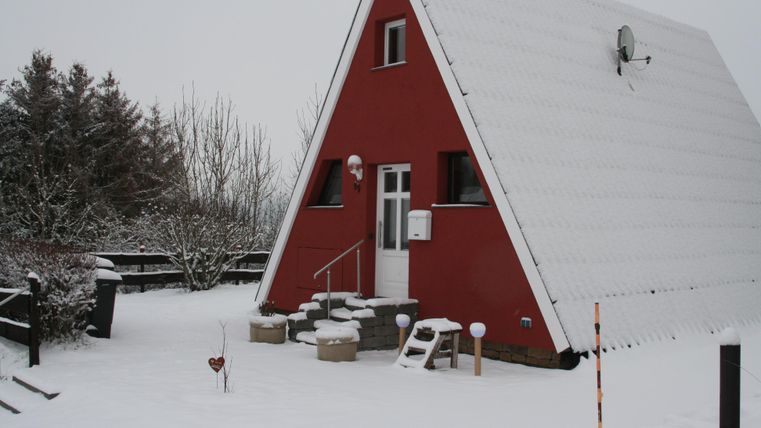 Une maison rouge de style A, entourée de neige fraîche. Le paysage est hiver et calme.