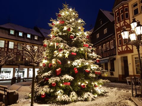 Ein festlich geschmückter Weihnachtsbaum steht im verschneiten Marktplatz. Die Lichter leuchten hell in der winterlichen Nacht.