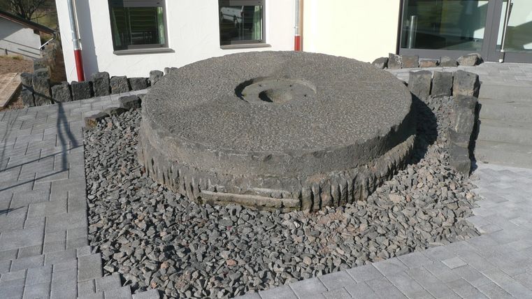 Grote molensteen op een grindbed voor een gebouw.