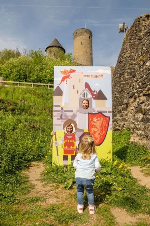 A child stands in front of a photo booth with knights and a dragon at the ruins of Nürburg Castle.