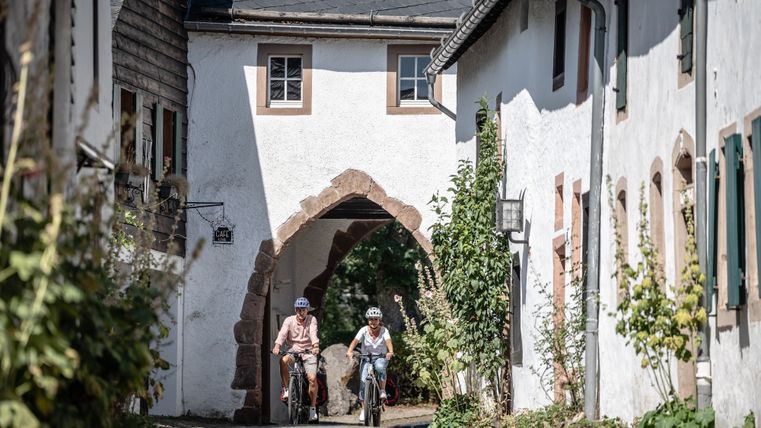 Twee fietsers met helmen rijden door een groep huizen in het historische kasteelstadje Kronenburg.