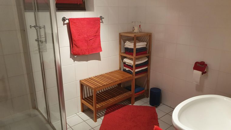 A modern bathroom with a shower and a wooden shelf.
