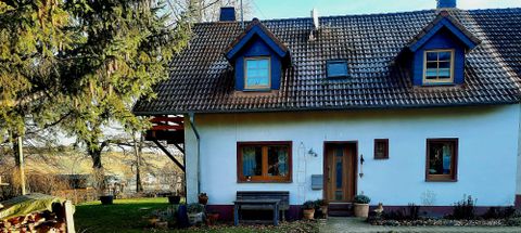 Een gezellig, twee verdiepingen tellend huis met een zadeldak en blauwe raamkozijnen. De ingang is omgeven door een kleine tuin.