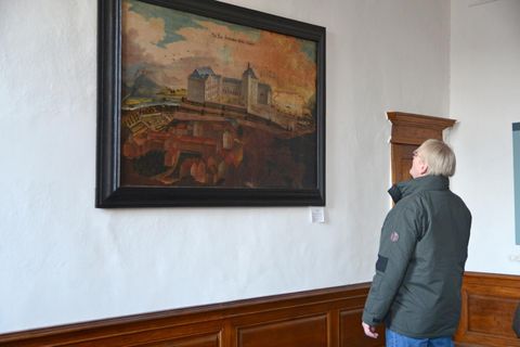 Een persoon bekijkt een schilderij aan de muur. De afbeelding toont een indrukwekkend landschap met historische gebouwen.