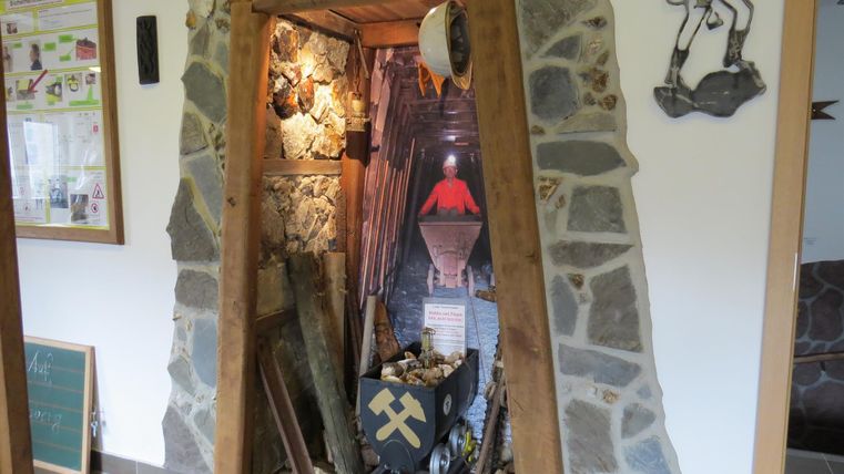 A decorative niche in natural stone style, reminiscent of a mine shaft. Inside, mining tools and a small trolley can be seen.