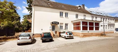 Un bâtiment avec plusieurs fenêtres et une zone couverte. Au premier plan, plusieurs voitures sont sur un parking.