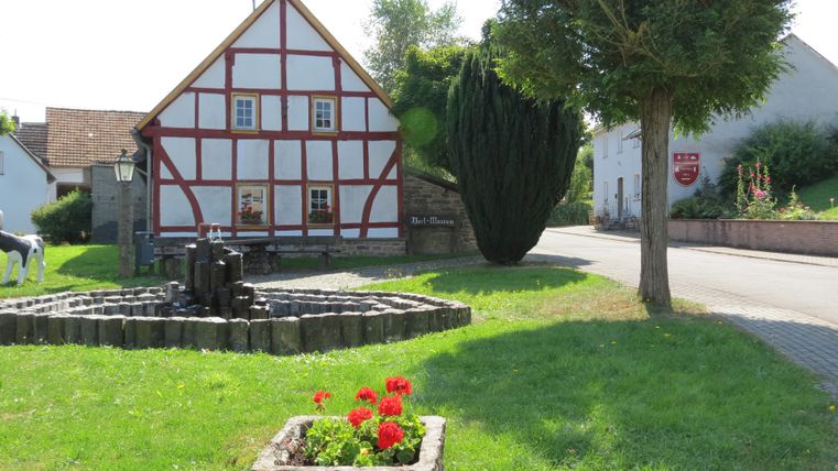 Half-timbered house with fountain and flower bed in the foreground.