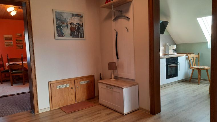 Un couloir lumineux avec un sol en bois et un petit coin salon. En arrière-plan, on voit un coin cuisine ouvert avec une plaque de cuisson.