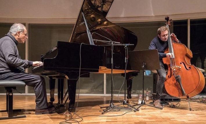 Two musicians are playing live on a stage. The pianist is sitting at the piano and the double bassist is standing next to him.