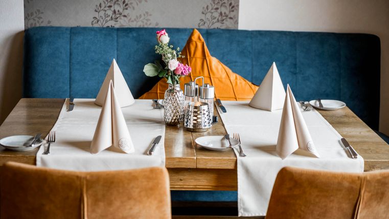 Een gedekte tafel in een stijlvol restaurant. De decoratie omvat elegante servetten, bestek en een bloemenvaas.