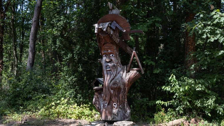 Wooden sculpture of a man with a saw in the forest.