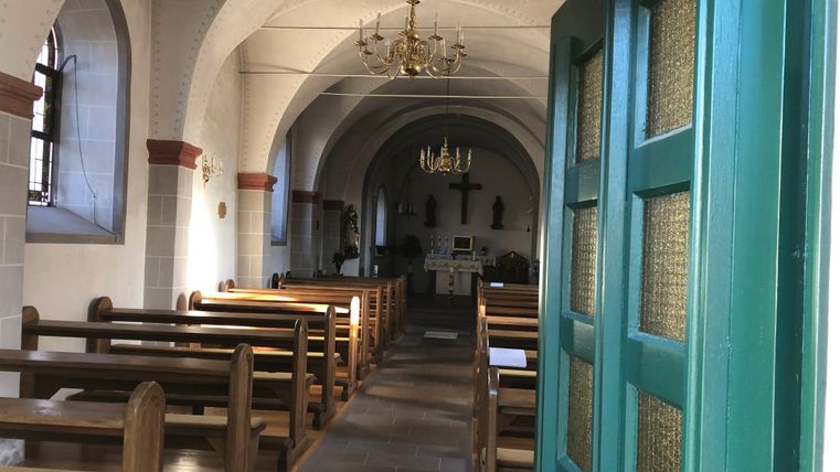 Binnenzicht van een kleine kapel met houten banken en een altaar op de achtergrond.