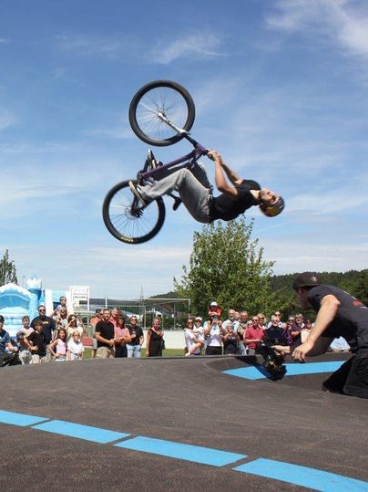 A BMX rider performs a spectacular backflip over a ramp. In the background, an enthusiastic crowd gathers to watch the performance.