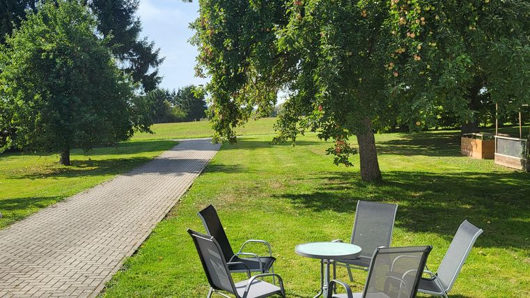 Een zonnige tuin met een tafel en stoelen. Op de voorgrond staat een blauwe zandbak met speelgoed.