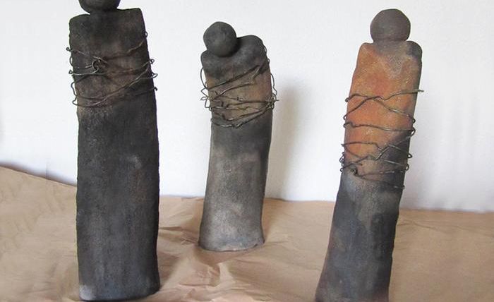 Three sculptural figures made of ceramic are standing on a table. They are in different shapes and colors, wrapped in wire.