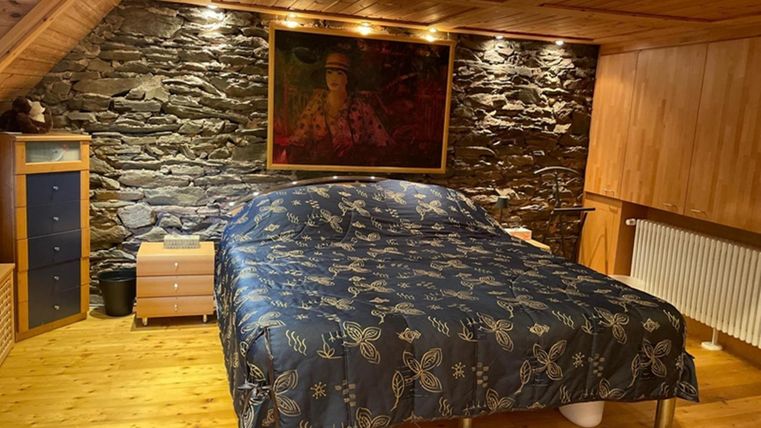 A cozy bedroom with a large bed and a blue duvet. The walls are panelled with stone and wood, and there is a large picture on the wall.