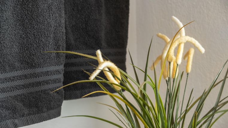 Een ontspannen badkamer sfeer met een zwart handdoek en een decoratieve plantenarrangement. De combinatie van textiel en plant element zorgt voor elegantie en gezelligheid.