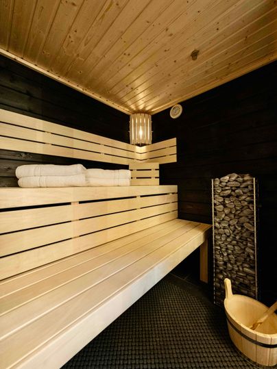 Ein gemütlicher Saunabereich mit Holzbanquettes und frischen Handtüchern. Neben der Liegefläche steht ein Holzbehälter und ein Steinregal.