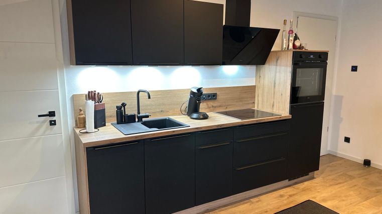 A modern kitchen in black and wood design. It is equipped with a sink, stove, and a microwave.