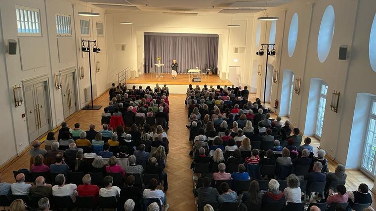 Ein voll besetzter Saal mit Hunderten von Menschen, die einem Vortrag lauschen. Auf der Bühne stehen zwei Personen, die im Gespräch sind.