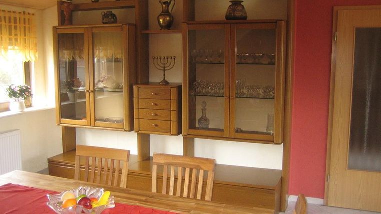 An inviting dining room with a wooden table and chairs. In the background, display cabinets are furnished with crockery and decorations.