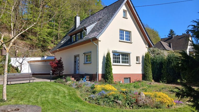 Ein schönes zweigeschossiges Haus mit einem gepflegten Garten. Umgeben von Bäumen und bunten Blumen strahlt es eine einladende Atmosphäre aus.