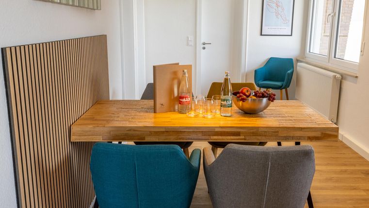 Een moderne eetruimte met een houten tafel en twee kleurrijke stoelen. Op de tafel staan een schaal met fruit en dranken.