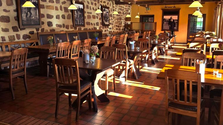 A cozy restaurant with wooden chairs and tables. Sunlight streams through the windows and brightens the room.