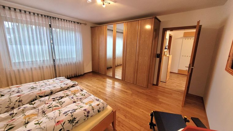 Ein helles Schlafzimmer mit zwei Betten und Holzboden. Der Raum verfügt über einen großen Kleiderschrank und Fenster mit Vorhängen.