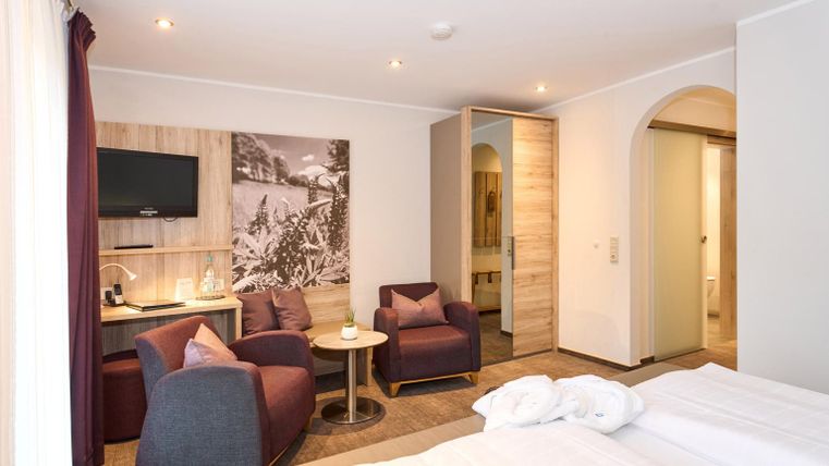 Een moderne hotelkamer met twee bedden en een zithoek. De muren zijn licht, en er is een televisie evenals uitzicht op een decoratief beeld.