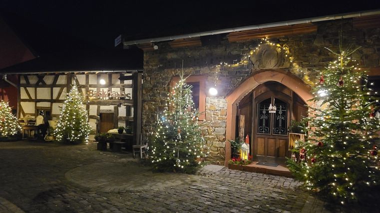 Une entrée magnifiquement éclairée d'un bâtiment en pierres traditionnelles. Entourée de sapins décorés, la scène dégage une ambiance chaleureuse de Noël.